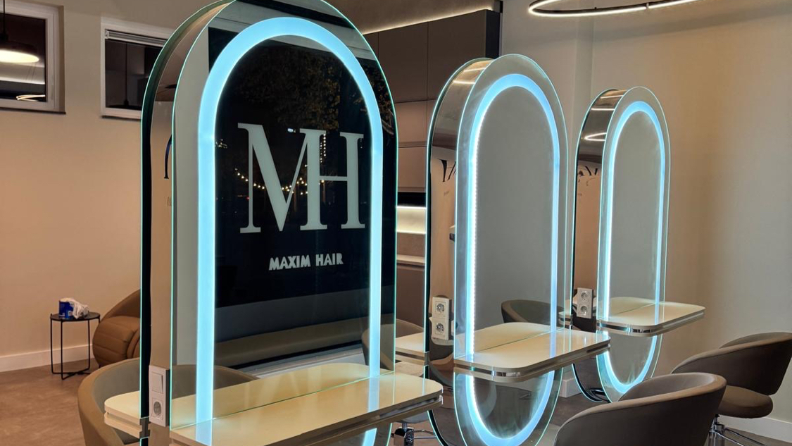 Spiegelwand met drie verlichte boogspiegels en het MH-monogram in de salon aan de Markt